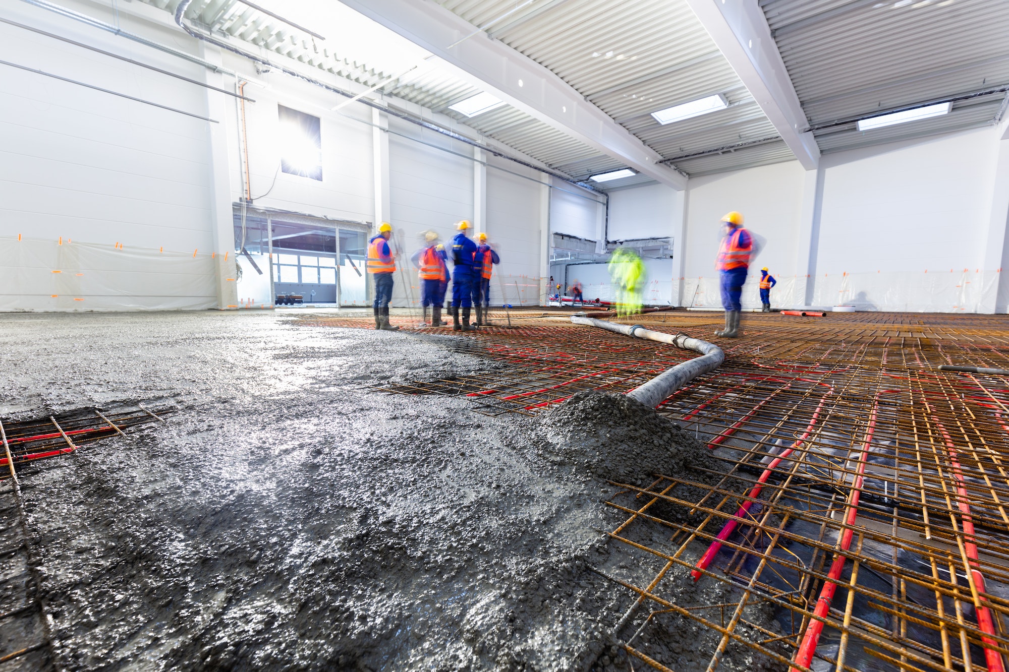 Workers do concrete screed on floor with heating in a new warehouse building